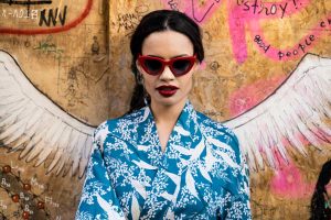 Mujer con gafas Mohikane rojas y chaqueta estampada, posando frente a un grafiti. Fotografia de producto en Vigo para e-commerce.